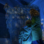 Adult and child look up at recreation of the Titanic's bow, illuminated by blue underwater lighting