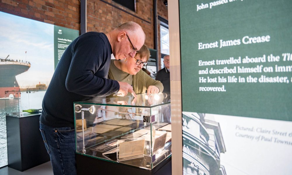 Titanic Bristol Visitors Two visitors peering into a glass cabinet with historic artefacts. Faces illuminated by LED information display boards